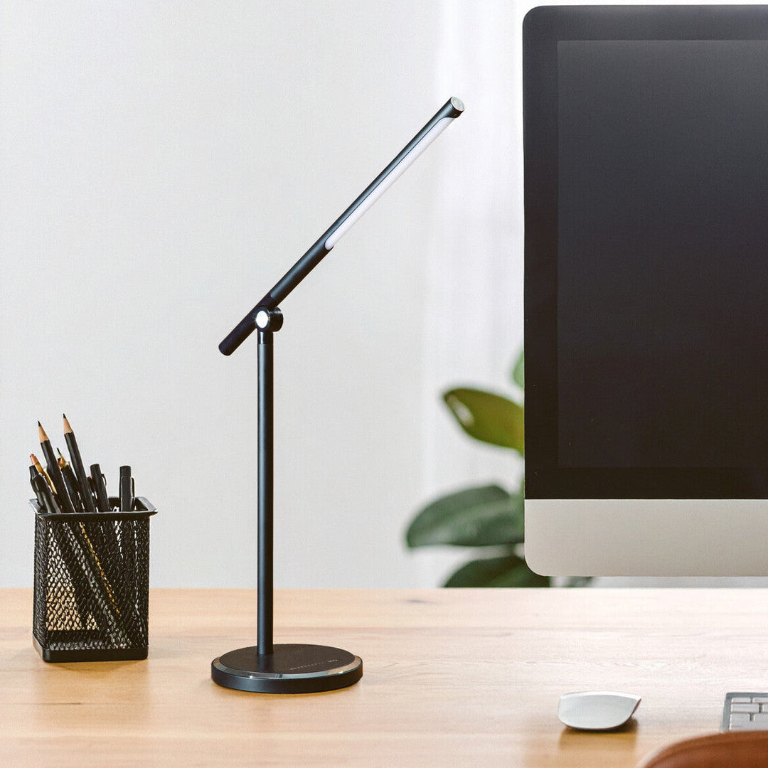 Desk setup with a computer monitor, lamp, and pen holder on a wooden desk.