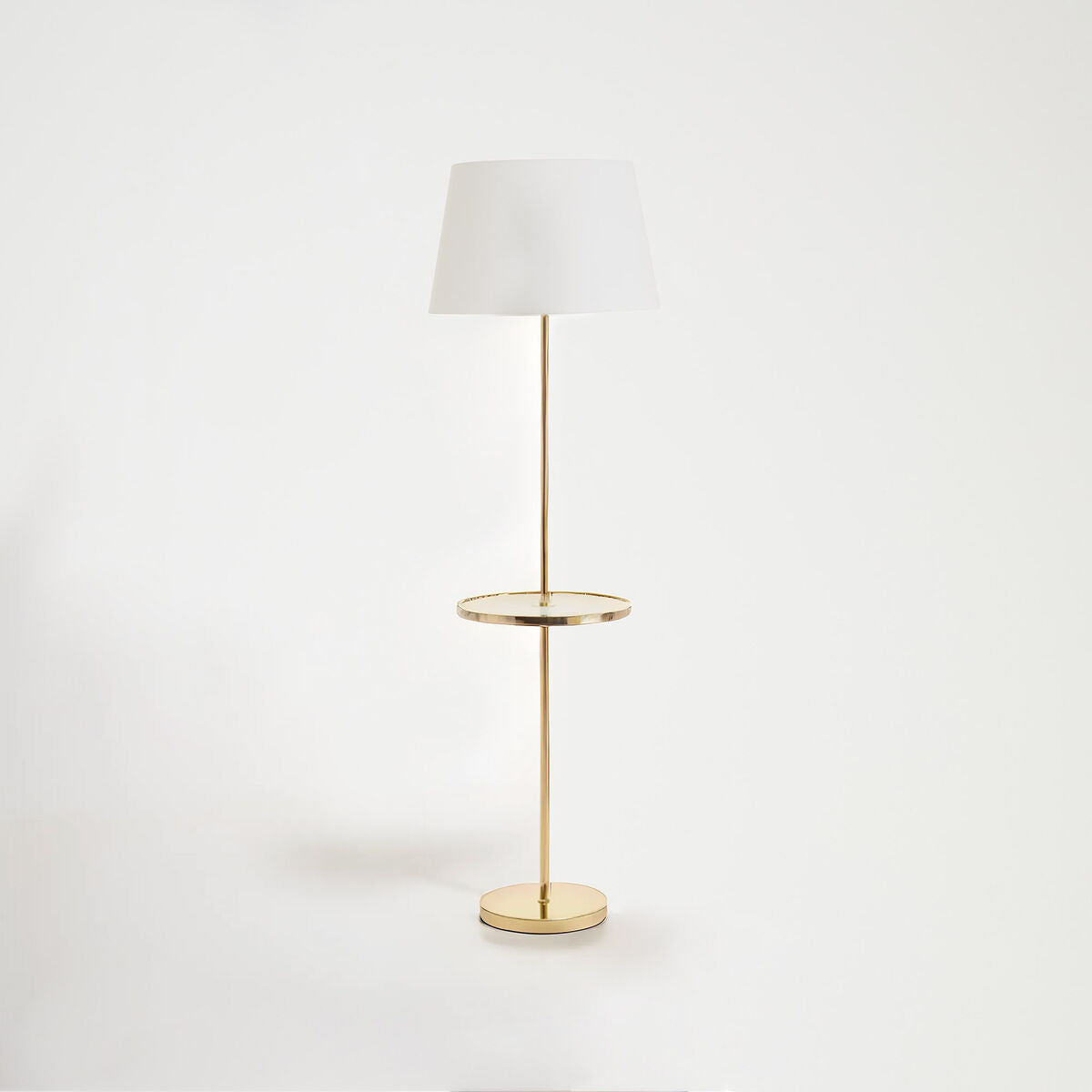 Floor lamp with a white shade and gold base on a light gray background