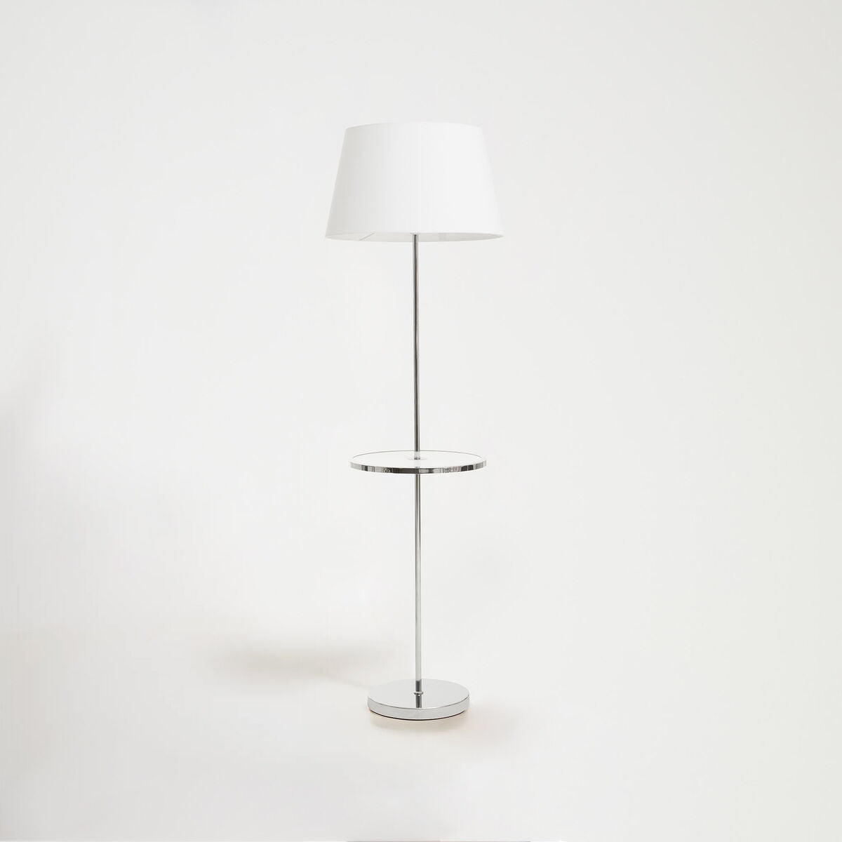 Floor lamp with a white shade and chrome base on a white background