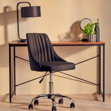 Modern office desk with black chair, lamp, and decorative items against a beige wall.
