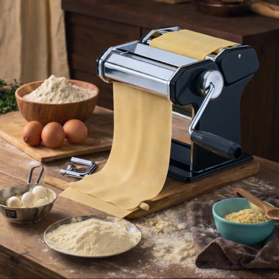 Pasta maker on a wooden table with ingredients, highlighting stainless-steel design.