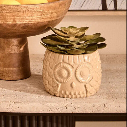 Wooden bowl with lemons on a table next to a small plant, with abstract art in the background.