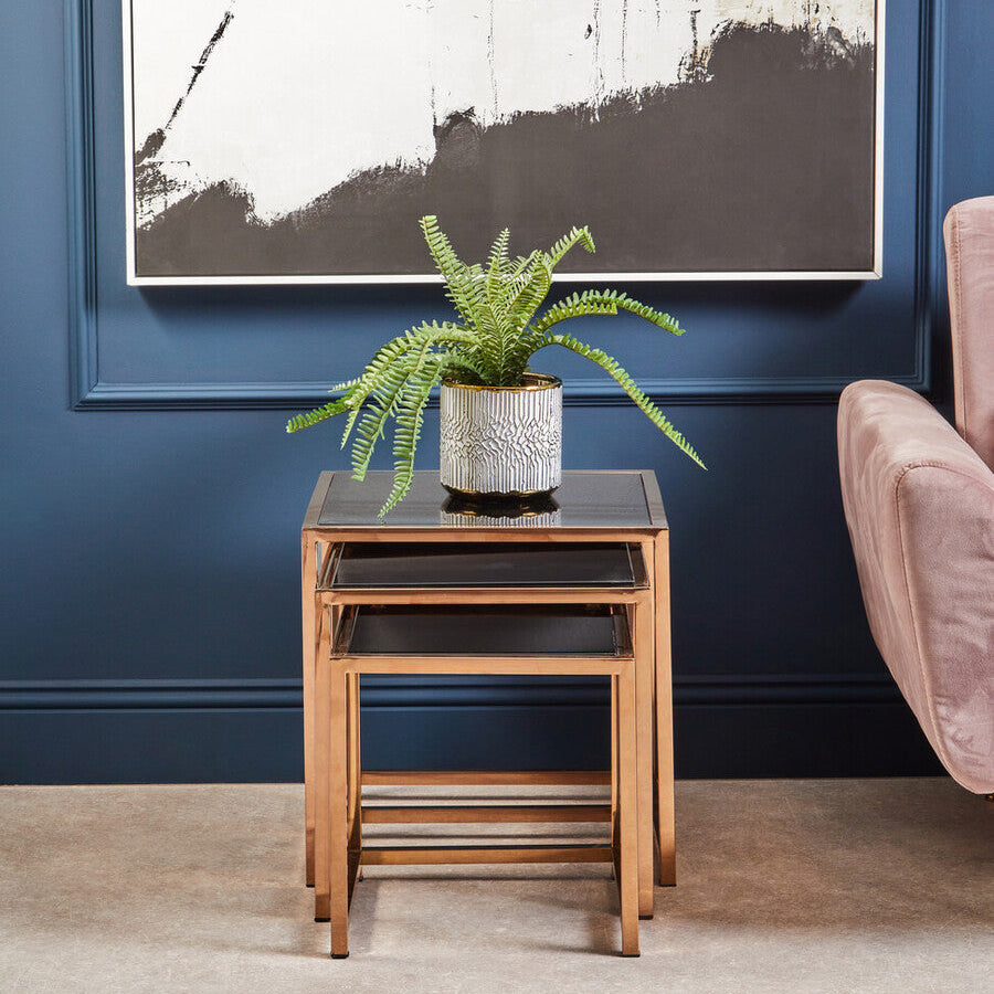 Nest of wooden tables with a potted plant against a blue wall with abstract art.