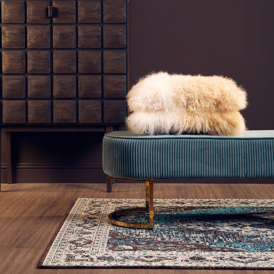 Fur-covered ottoman on a teal sofa with a wooden cabinet and decorative items in the background.