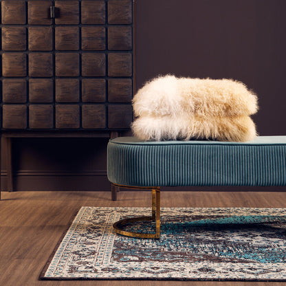 Fur-covered ottoman on a teal sofa with a wooden cabinet and decorative items in the background.