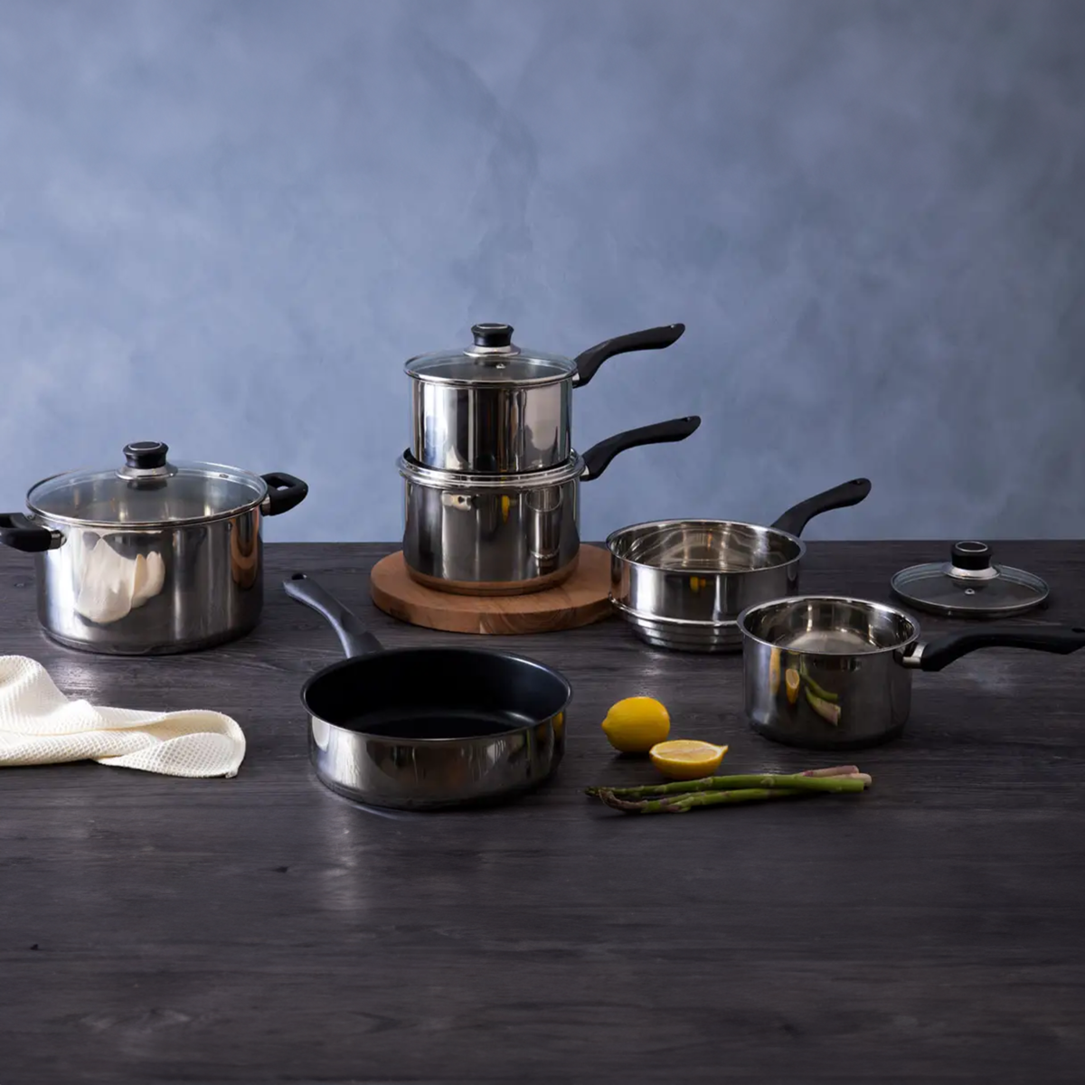 Set of stainless steel cookware on a dark surface with a blue background