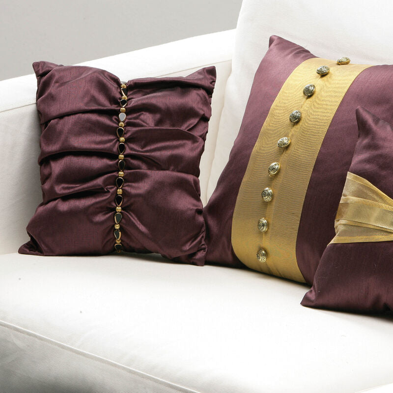 Three decorative pillows with gold accents on a white couch.