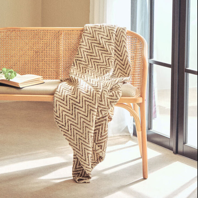 Wicker bench with a patterned throw blanket in a bright room with large windows.