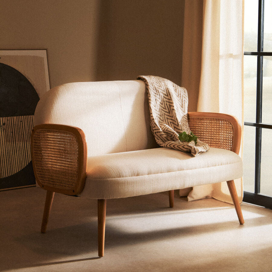 Beige sofa with wicker armrests in a room with soft lighting