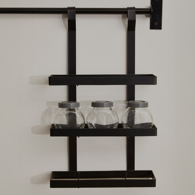 Black metal wall shelf with three glass jars on a plain background