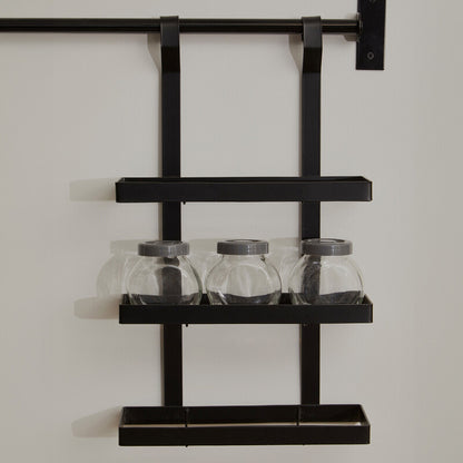 Black metal wall shelf with three glass jars on a plain background