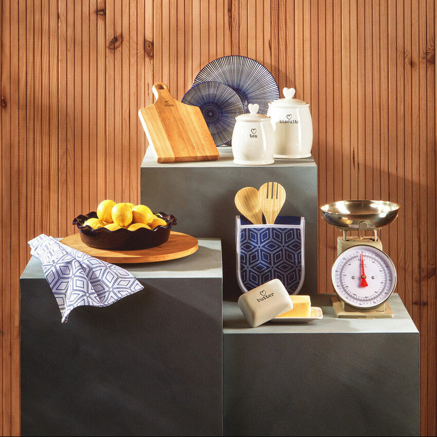 Kitchen counter with various items including a bowl of lemons, cutting board, and kitchen scale against a wooden wall.