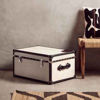 White storage trunk with black accents on a gray floor next to a chair with a cowhide pattern.