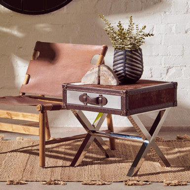 Brown leather chair and side table with a vase of flowers against a white brick wall.