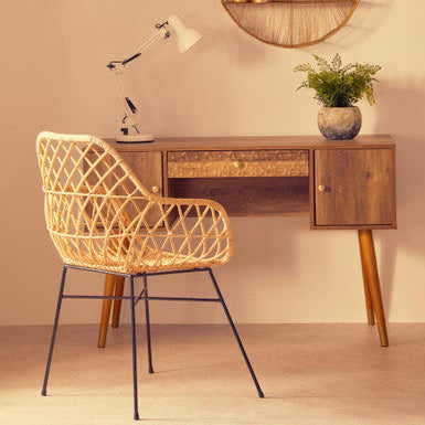 Wooden desk with wicker chair and round wall shelf in a room.