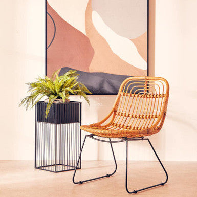 Wicker chair next to a plant in a decorative pot against a abstract wall art background
