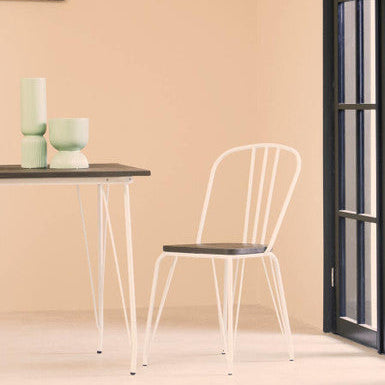 White chair and small table against a beige wall with a black-framed mirror.