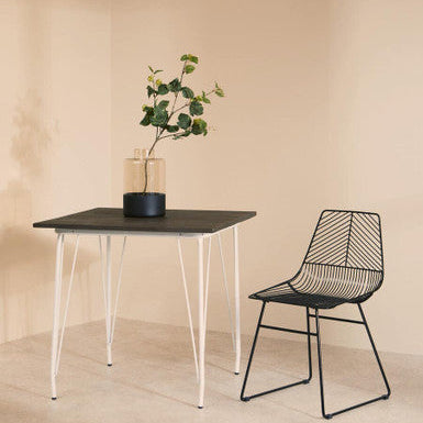 Black dining table with white legs and a black chair against a beige wall.
