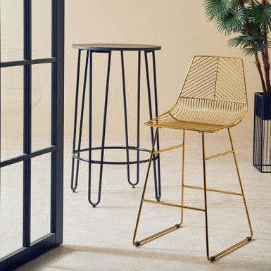 Gold wire bar stool and black metal bar stool against a beige wall with a plant.
