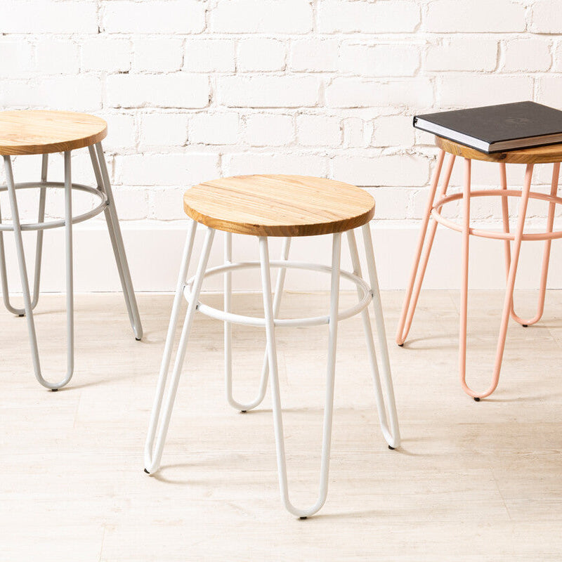 Three stools with different designs and colors against a white brick wall.