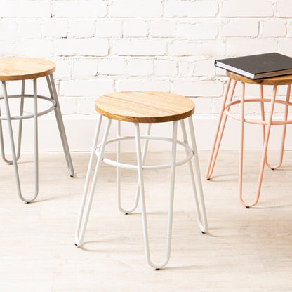 Three stools with different designs and colors against a white brick wall.