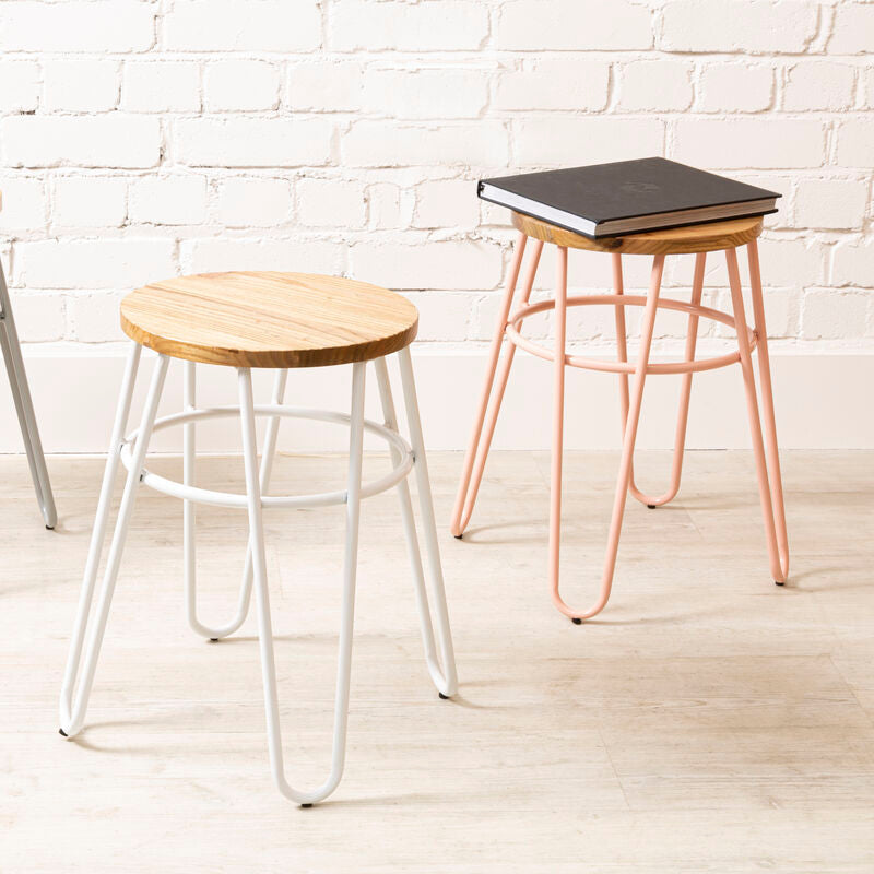 Three stools with different designs and colors against a white brick wall.