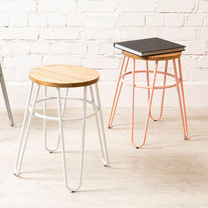 Three stools with different designs and colors against a white brick wall.