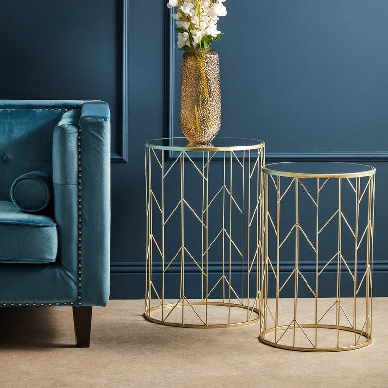 Gold wire side tables with a vase of flowers against a blue wall.