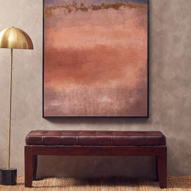 Abstract painting on a wall above a brown leather bench with a gold floor lamp.