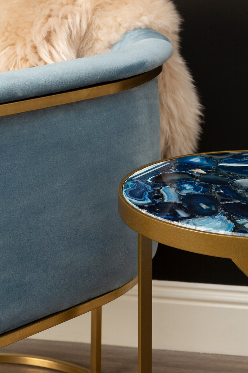 Blue velvet chair with a gold frame next to a round side table with a blue marbled design.