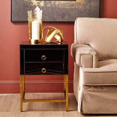 Black and gold side table with decorative items next to a beige armchair against a red wall.