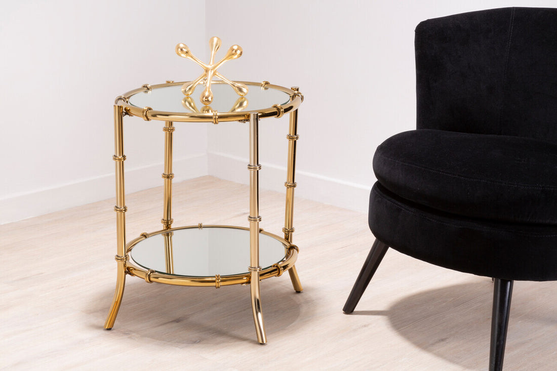Gold side table with glass shelves next to a black chair on a white background