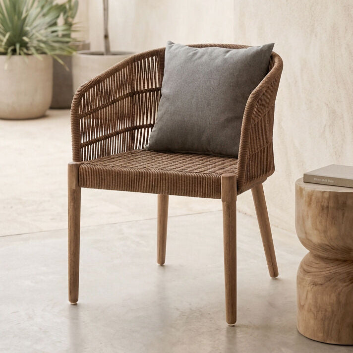 Wicker chair with a gray cushion next to a wooden side table in a room with plants.