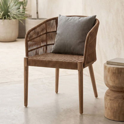 Wicker chair with a gray cushion next to a wooden side table in a room with plants.
