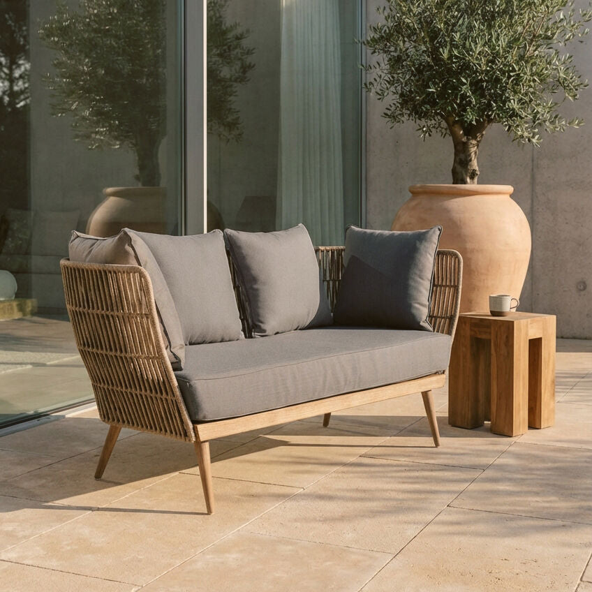 Outdoor patio set with wicker sofa and wooden side table on a stone patio.