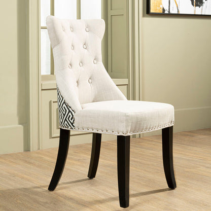 White upholstered chair with black legs in a room with wooden flooring and a window.