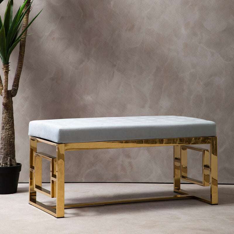 Modern bench with gold frame and white cushion next to a potted plant against a textured wall.