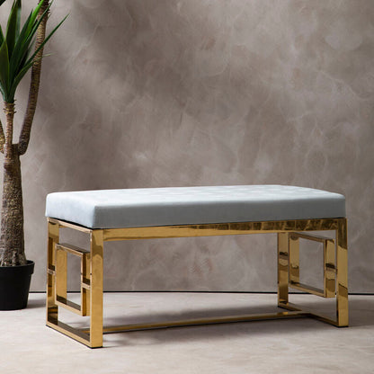 Modern bench with gold frame and white cushion next to a potted plant against a textured wall.