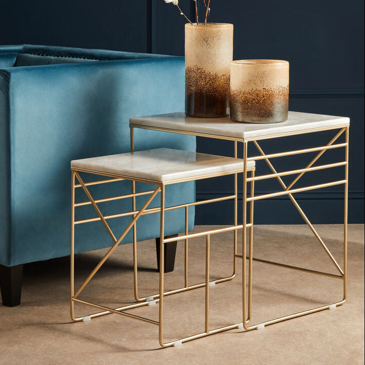 Modern gold side table with marble top next to a blue sofa against a dark wall.