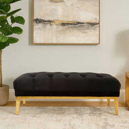 Black tufted bench with wooden legs in a room with abstract art and plant.