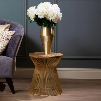 A gold wire side table holding a matching gold vase filled with white flowers, styled next to a purple armchair in a room with dark paneled walls and wood flooring.