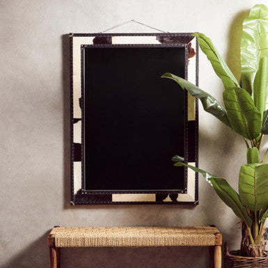 Decorative mirror with wicker bench and plant on a patterned rug