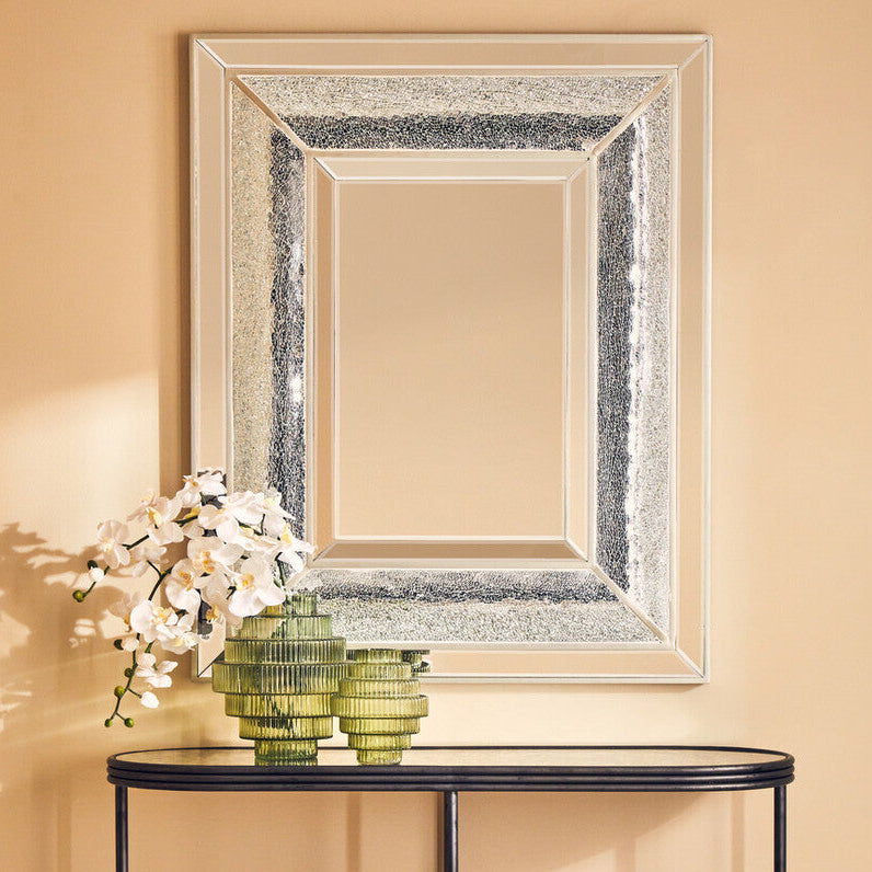 Console table with decorative mirror and flowers against a beige wall