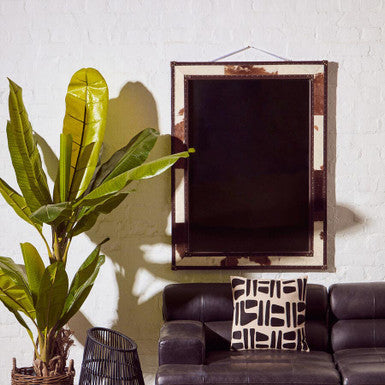 Living room with a brown leather sofa, decorative pillow, plant, and mirror on a white wall.