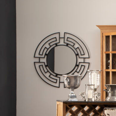 Decorative mirror with geometric design on a wall above a wooden cabinet with glass doors.