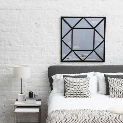Modern bedroom with white brick wall, bed with patterned bedding, and geometric mirror.