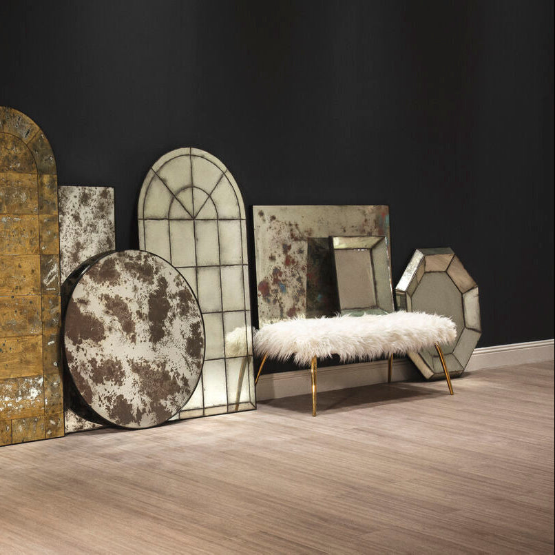 Decorative mirrors and a bench on a wooden floor against a dark wall.