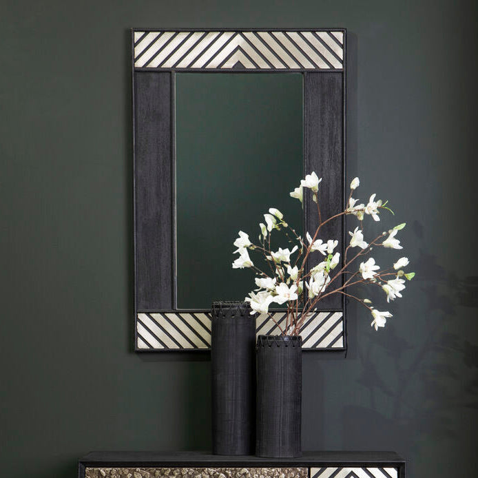 Black cabinet with geometric design, mirror, and vase with white flowers on a dark wall.