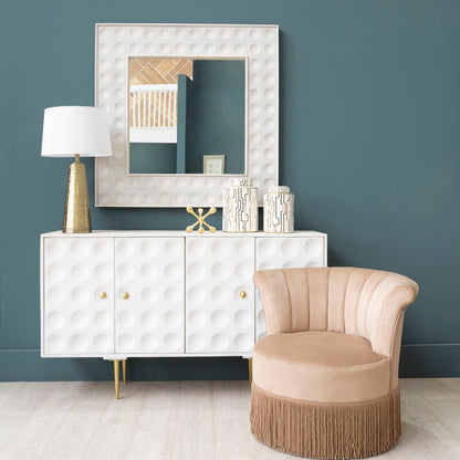 Modern interior with a white sideboard, beige chair, and decorative mirror against a dark blue wall.