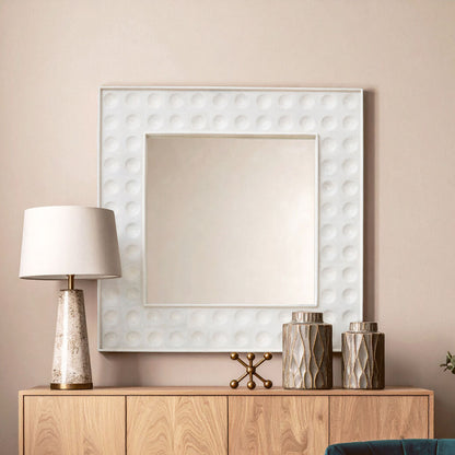 Decorative mirror with textured frame above a wooden cabinet with a lamp and decorative items.